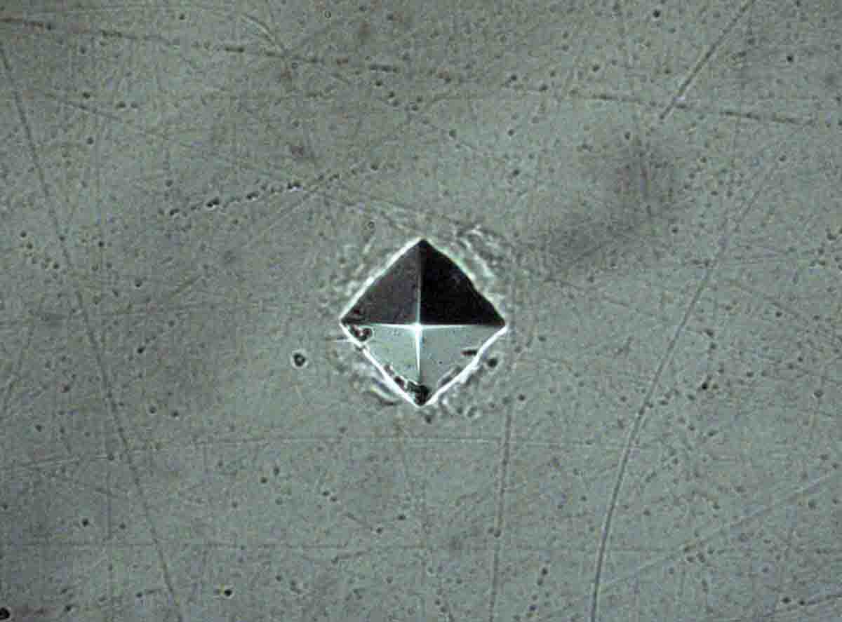 This is a fully-lit indent in a brass sample to illustrate the pyramid shape of the indenter, magnified 500 times.